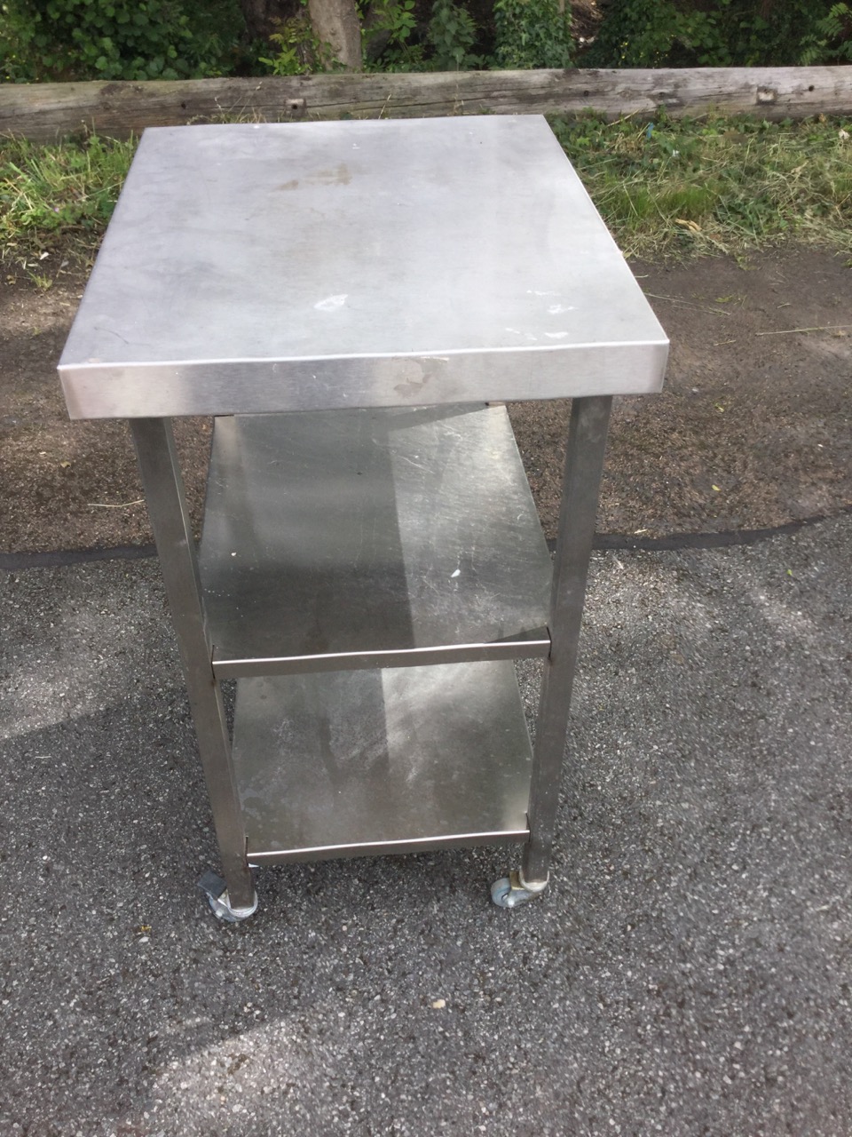 A rectangular stainless steel table with two shelves below, raised on casters. (23.5in x 19.5in x