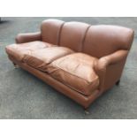 A contemporary leather three-seater sofa, with three arched back above loose cushions, having padded