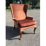 A Parker Knoll wingback armchair having padded arms above a sprung seat with loose cushion, raised