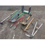 A quantity of garden tools including a rake, a pick axe, spades, a branch loper, a stool, shears,