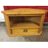 A pine corner unit with canted platform top above an open compartment and panelled drawer, raised on