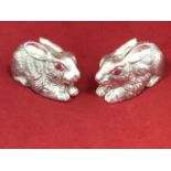 A pair of silver plated rabbit salt & pepper pots, the prone animals with ruby style glass eyes. (