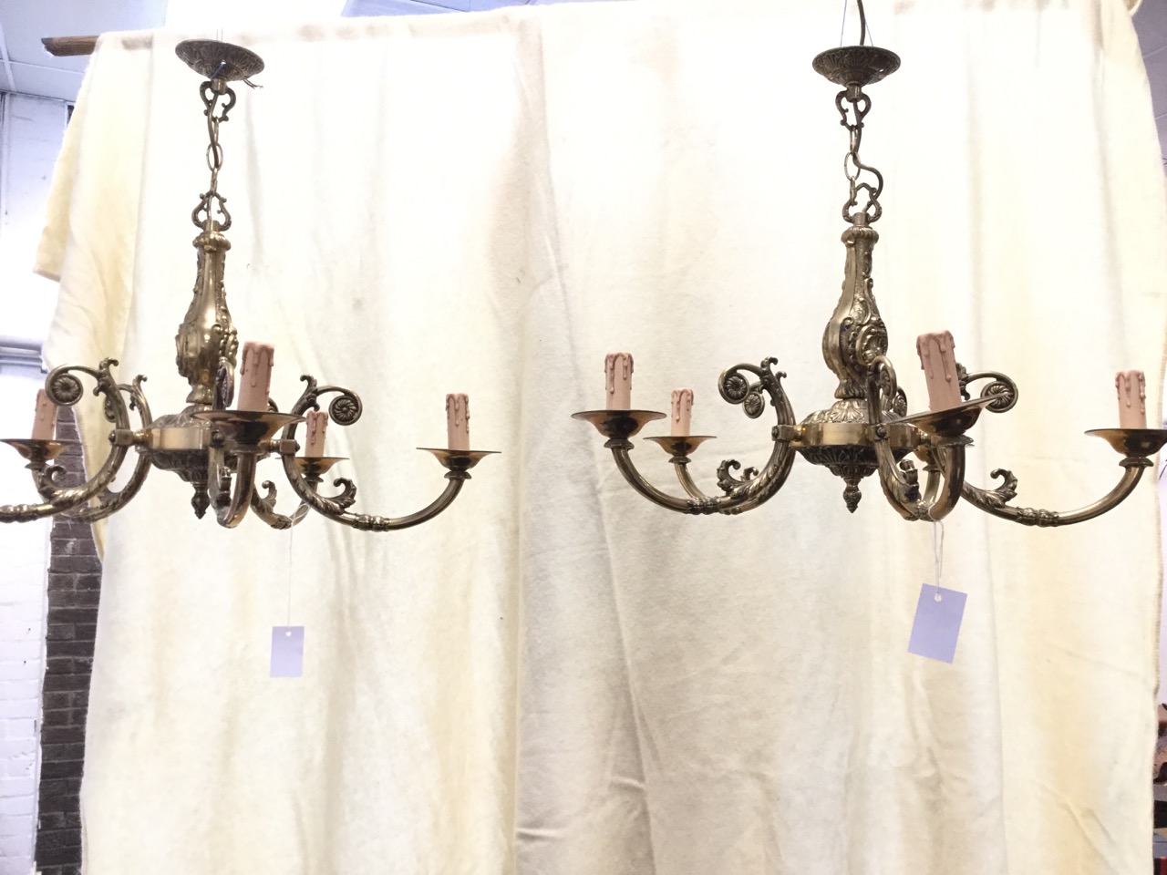 A pair of brass chandeliers with scrolled cast columns suspended with chains from ceiling roses,