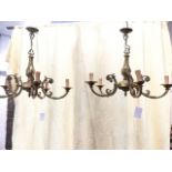 A pair of brass chandeliers with scrolled cast columns suspended with chains from ceiling roses,