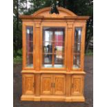 A glazed architectural display cabinet, with broken scroll carved pediment above a cornice with