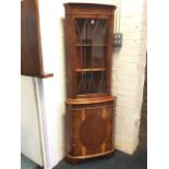 A bowfronted yew corner cabinet, with moulded dentil cornice above an astragal glazed door enclosing