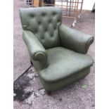 An Edwardian button upholstered armchair with flared arms above a sprung seat, raised on turned