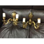 A pair of heavy brass wall lights, the ribbed wallplates supporting twin scrolled branches with
