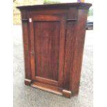 A Georgian oak corner cupboard with moulded cornice above a crossbanded panelled door enclosing an