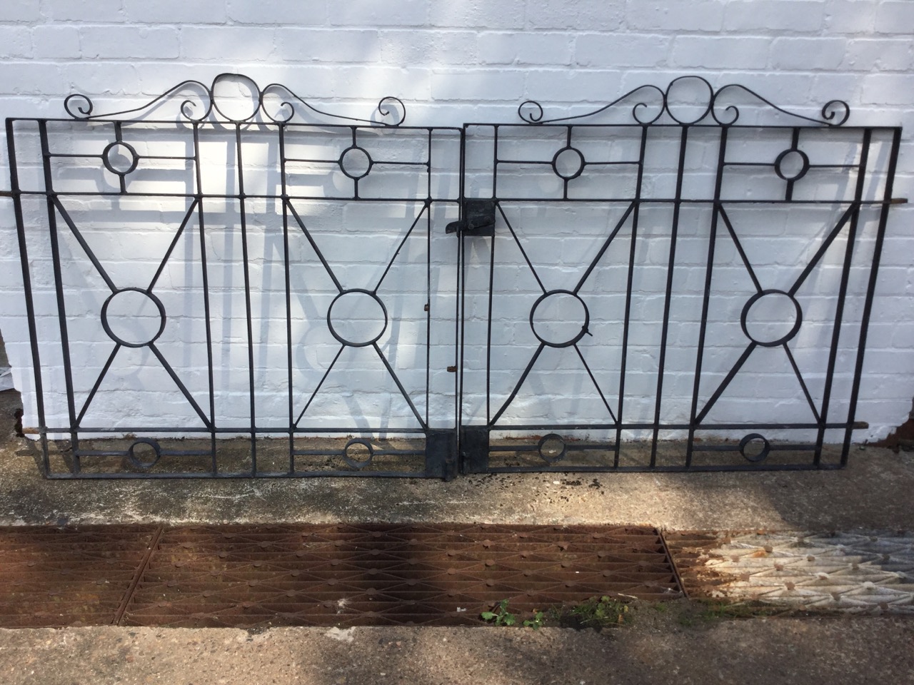 A pair of wrought iron driveway gates with scrolled crests above rectangular panels centred by