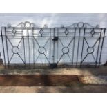 A pair of wrought iron driveway gates with scrolled crests above rectangular panels centred by