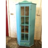 A painted pine corner cupboard with arched crest above a glazed door enclosing shelves, having