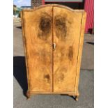 A 1950s walnut compactum with chisel carved arched top above two doors enclosing a fitted interior