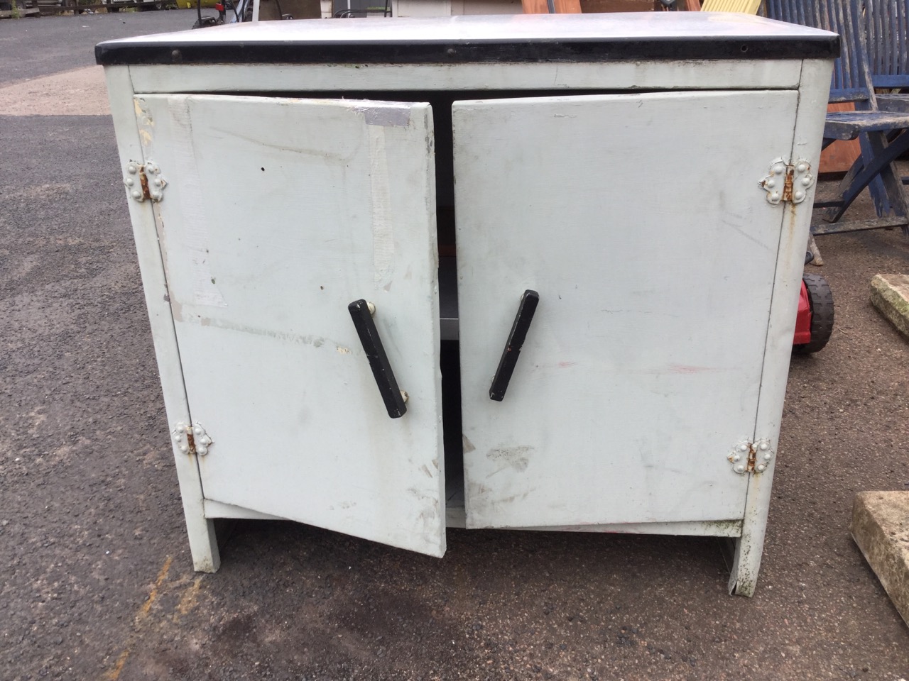 A kitchen cabinet with rectangular enamelled top above a rounded painted aluminium cupboard with two