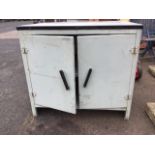 A kitchen cabinet with rectangular enamelled top above a rounded painted aluminium cupboard with two