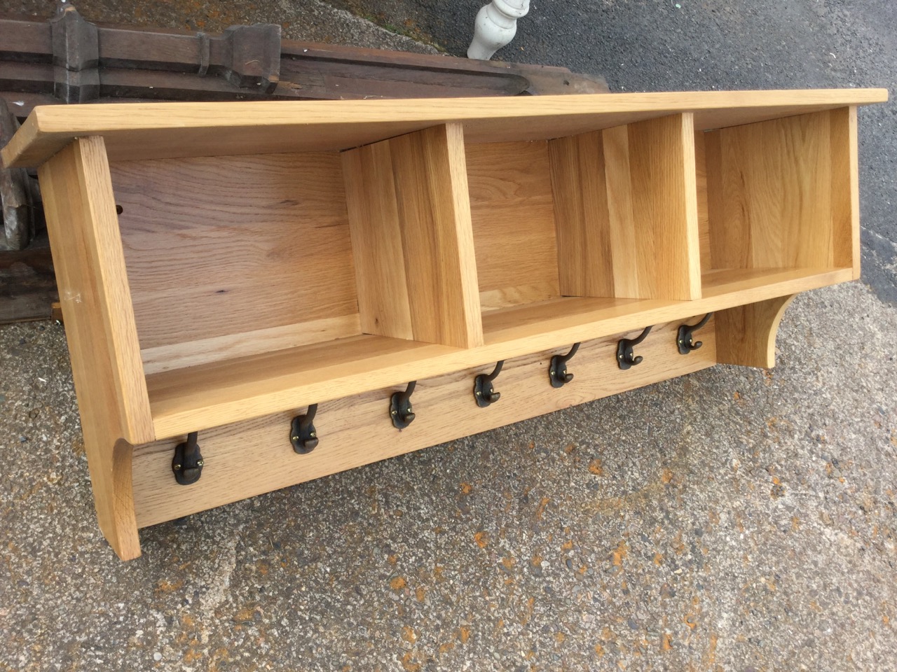 A contemporary oak hall rack, with shelf above three open compartments, having row of seven brass