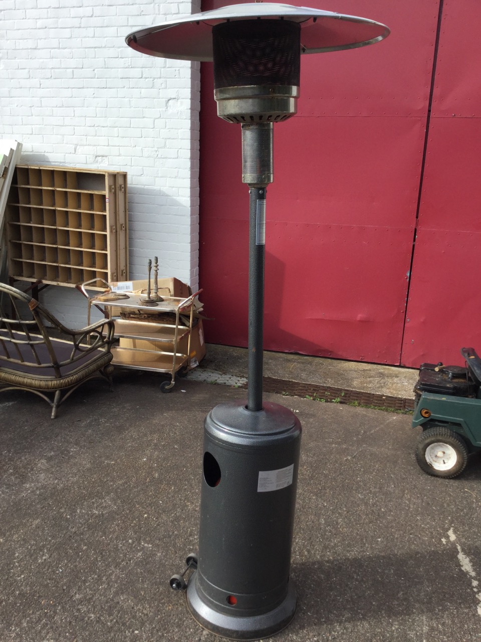 A gas patio heater with gauze reflector on column above a tubular base on casters, complete with a