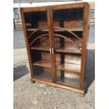 A deco oak bookcase with rounded top above arched glazed doors mounted with chrome handles enclosing