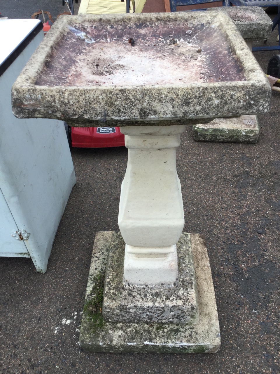 A composition stone birdbath, with square basin on later column, above a stepped plinth base. (