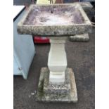A composition stone birdbath, with square basin on later column, above a stepped plinth base. (