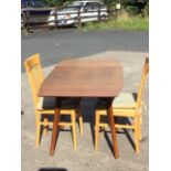 A 60s mahogany dining table and pair of dining chairs, the table with tapering drop-leaves on angled
