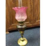 A Victorian oil lamp with waved cranberry acid etched shade above a cut glass reservoir, on a