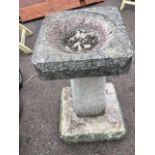 A composition stone birdbath with square basin on naturalistic tapering column above a plinth. (