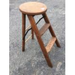An early C20th folding oak ladder stool, the circular top above two treads with hinged iron stays,