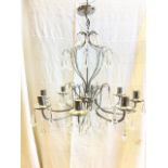 A contemporary chrome hanging chandelier with eight branches holding candlelamp fittings above