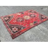 An oriental rug woven with three joined octagonal serrated medallions on madder field with