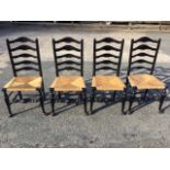 A set of four ebonised ladderback dining chairs, the arched backs above rush seats, raised on turned