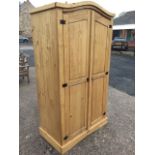 An arched pine wardrobe with two fielded panelled doors enclosing shelf and hanging space, the doors