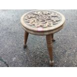 A carved circular mahogany three-legged stool, the seat with floral medallion framed by stylised