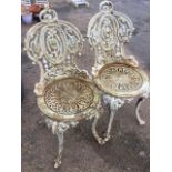 A pair of heavy Victorian cast iron garden chairs, the ornate pierced backs with oval panels above