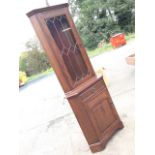 An oak corner cupboard having illuminated interior, the door with leaded glass having press carved