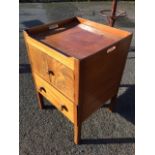 An antique mahogany bedside cabinet with later alterations, the tray top with handholes above a pair
