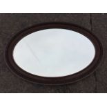 An Edwardian oval mirror in grained concave moulded frame with applied gesso decoration, the inner