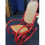 A painted bentwood rocking chair with rounded cane back and seat on scrolled supports with shaped