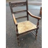 A carved oak armchair with floral ladderback rails and shaped arms on spindles above a rush seat,
