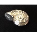 A silver pill pot modelled as a conk shell with embossed scrolled decoration, the hinged cover in