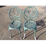 A pair of metal garden chairs with spade shaped scrolled backs above circular seats, raised on
