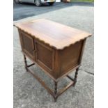 A rectangular oak cabinet with scalloped lifting top above beaded panelled doors, raised on