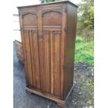 A carved oak wardrobe with moulded cornice above linenfold panelled doors, enclosing a fitted