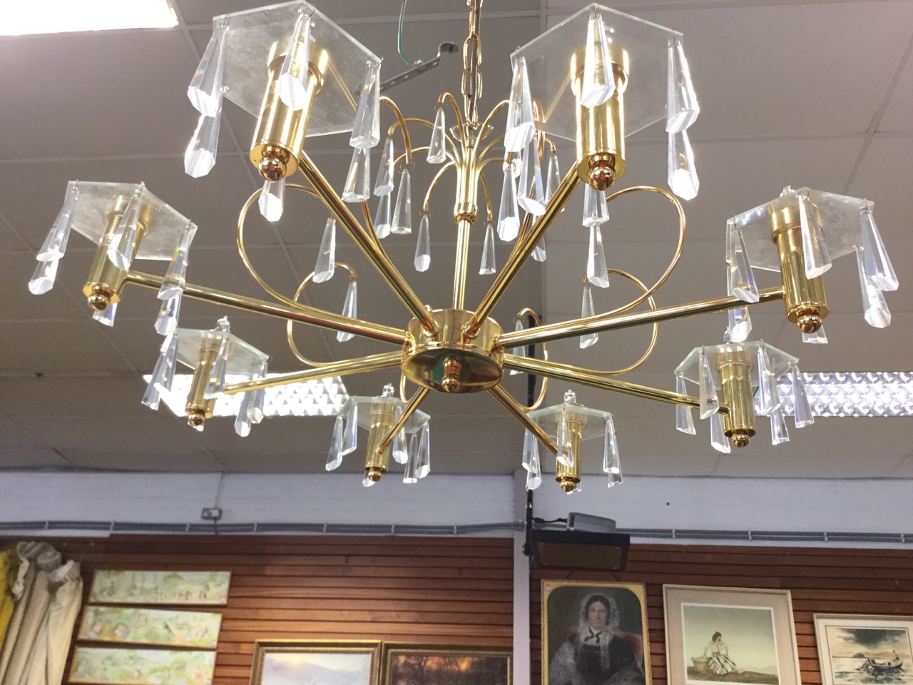 A contemporary brass chandelier supported by chain from ceiling rose, the column with boss