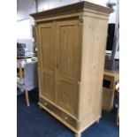 A European pine wardrobe with moulded cornice above panelled doors enclosing shelves, framed by