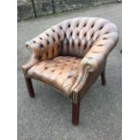 A leather upholstered armchair with button upholstery, the tub shaped back with brass studding