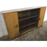 A 50s walnut bookcase with sliding glass doors flanked by cupboards, raised on plinth. (53.5in x