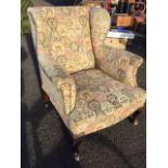 An upholstered mahogany wingback armchair with padded back and arms above a sprung seat, having