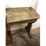 An Edwardian oak school desk with angled hinged lid in front of penrest and inkwell, raised on