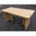 A rectangular pine table with thick plank top on T-shaped supports. (63in x 31.5in x 29.75in)